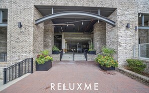 Entrada de un edificio de ladrillo con un corredor cubierto, plantas en macetas y un cartel que dice "RELLUXME".