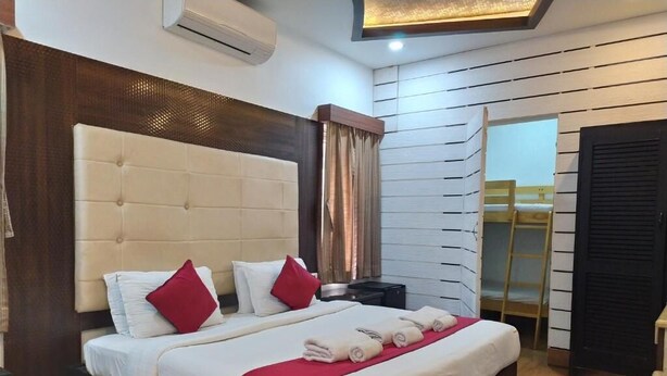 A neatly made bed with white bedding and red pillows, a wooden headboard, and a bedside table with a lamp. - HOTEL GRAND PARKWAY (Chennai)