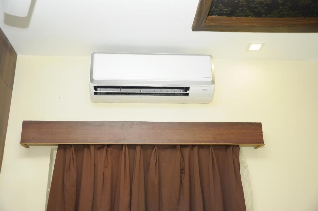 Un equipo de aire acondicionado blanco montado en la pared, sobre un panel de madera y cortinas marrones.