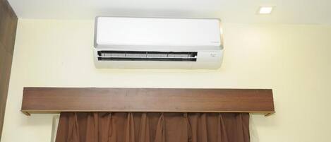 Un equipo de aire acondicionado blanco montado en la pared, sobre un panel de madera y cortinas marrones.