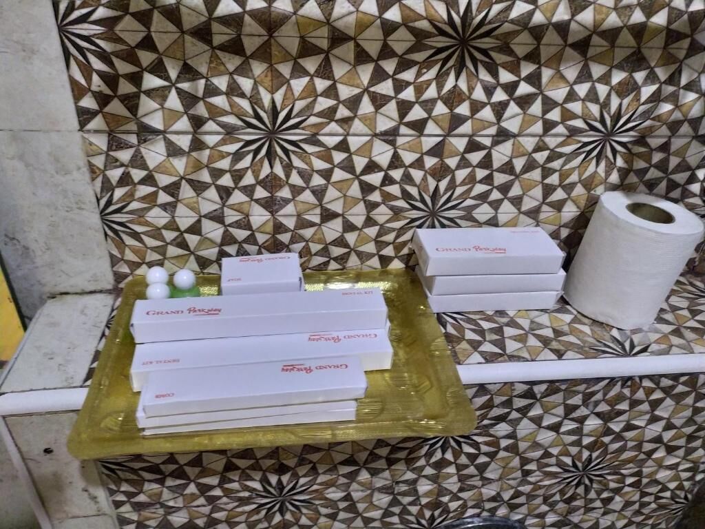 A bathroom with patterned tiles, a roll of toilet paper, and a tray with boxes labeled "Creamy Prosecco."