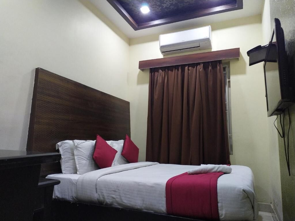 Habitación de hotel con cama, cabecera de madera, televisión de pantalla plana, lámpara de techo y equipo de aire acondicionado.