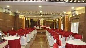 A banquet hall with rows of round tables, each covered with white tablecloths and red chair covers. The room has a polished floor and wooden paneling on the walls. - HOTEL GRAND PARKWAY (Chennai)