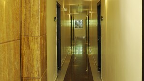 A corridor with marble walls and a reflective floor, leading to a door with a frosted glass panel. - HOTEL GRAND PARKWAY (Chennai)