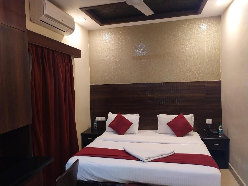 Una habitación de hotel con cama, dos mesitas de noche, cortina roja y ventilador de techo.