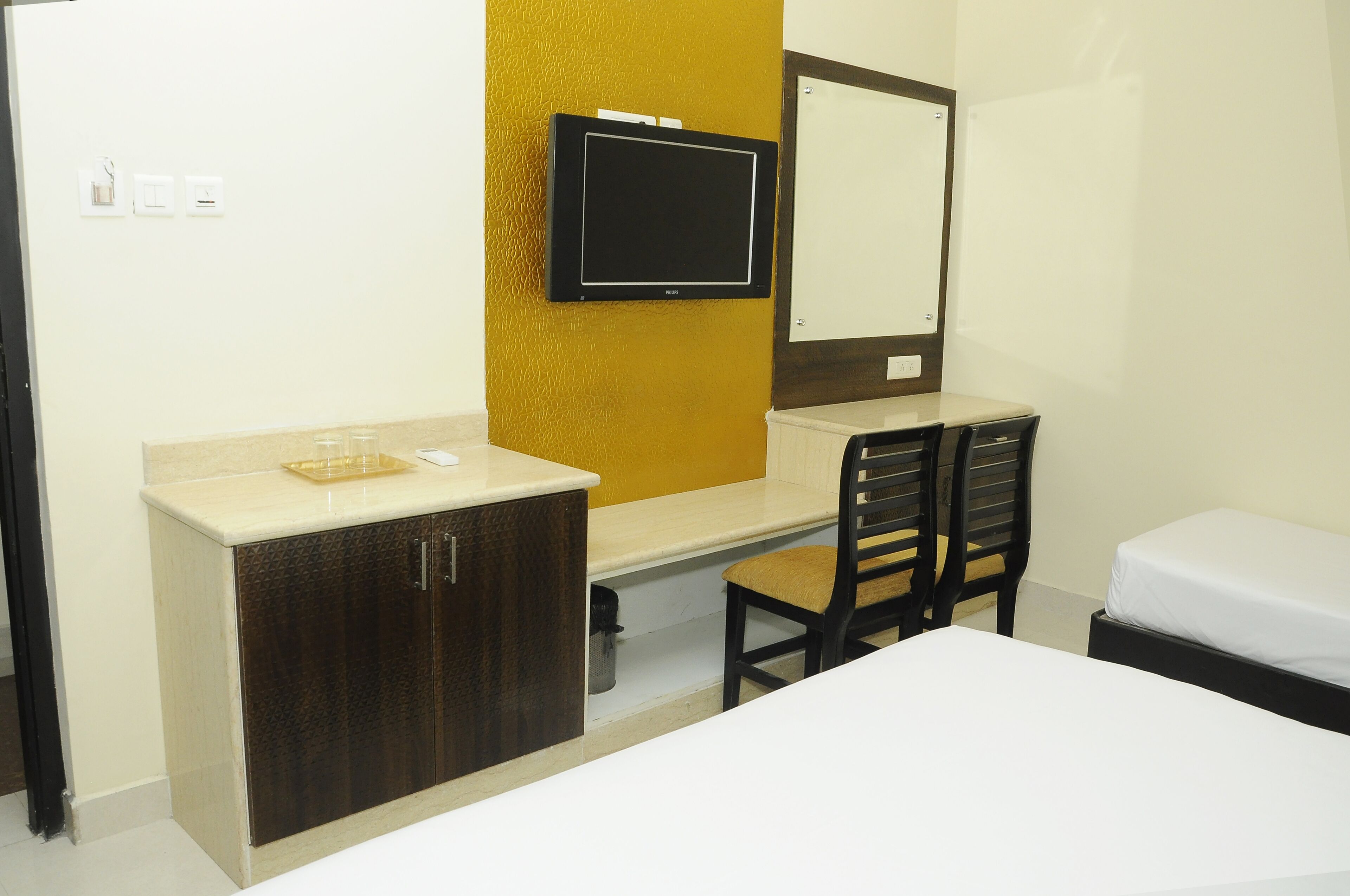 Habitación de hotel con cama, escritorio con silla, televisor montado en la pared y una ventana pequeña.