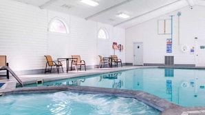 An indoor swimming pool with clear water, surrounded by white walls and multiple seating areas. - Canberra Premiere Comfort Hotel (Mackinaw City)