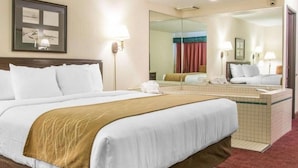 A hotel room with a large bed, a bedside table, a mirror, a bathroom with a sink, and a shower. - Canberra Premiere Comfort Hotel (Mackinaw City)