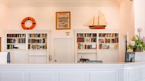 A reception area with a white counter, bookshelves, a life ring, a framed sign, and a ship model. - Canberra Premiere Comfort Hotel (Mackinaw City)