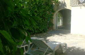 A patio area with two white plastic chairs and a concrete floor.