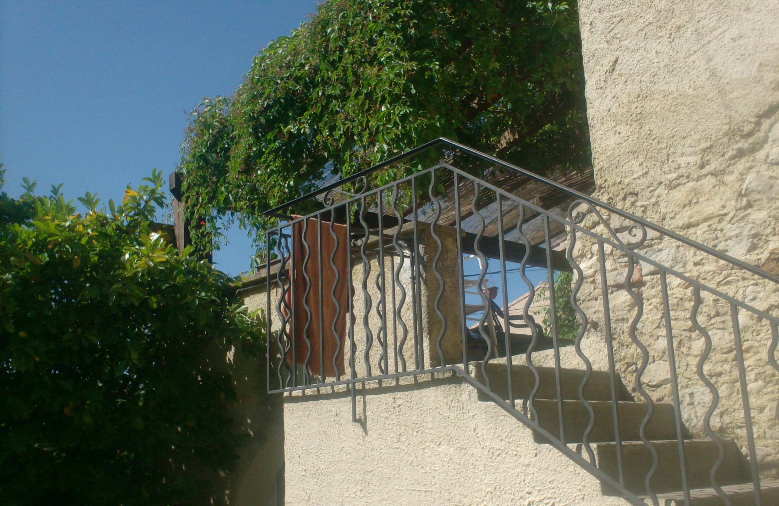 A staircase with metal railings leading up to a door, surrounded by greenery and a clear blue sky.