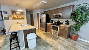 A modern kitchen with a central island, stainless steel appliances, and a potted plant. - Juniper Townhouse #4 (Mitchell)