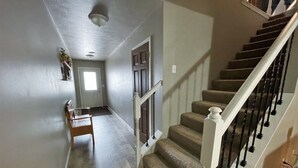 A hallway with a wooden bench, a door, and a staircase with a white balustrade. - Juniper Townhouse #4 (Mitchell)
