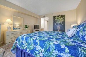 A bedroom with a bed, a dresser, a television, a lamp, and a painting. - Steps to the Beach! Rocket Launch View Condo (Cocoa Beach)