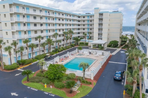 A multi-story hotel with a swimming pool, palm trees, and a view of the ocean.