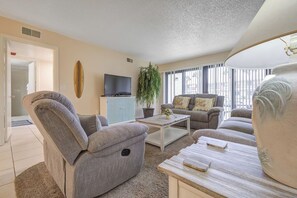 A living room with a sofa, armchair, coffee table, television, and a potted plant. - Steps to the Beach! Rocket Launch View Condo (Cocoa Beach)