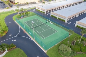 An aerial view of a tennis court surrounded by a parking lot and buildings.