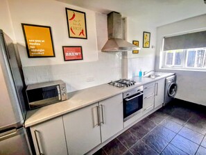 Une cuisine moderne avec des armoires blanches, une cuisinière à gaz, un four à micro-ondes et un four encastré. Des tableaux encadrés ornent le mur, et une fenêtre laisse entrer la lumière naturelle.
