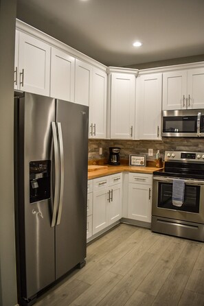 A modern kitchen with white cabinets, stainless steel appliances, a wooden countertop, and a tiled backsplash.