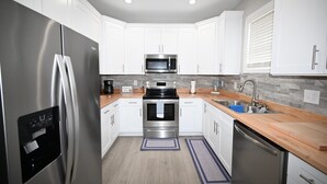 A modern kitchen with white cabinets, stainless steel appliances, a wooden countertop, and a built-in oven.