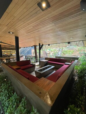 A modern outdoor seating area with wooden benches and red cushions, surrounded by greenery and a view of a natural landscape. - Hotel Oxú (Valle de Bravo)