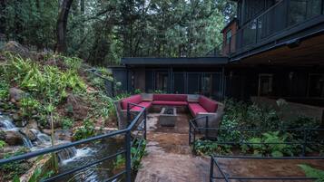 Un área de descanso moderna al aire libre con fuente de agua, rodeada de abundante vegetación y una terraza de madera.