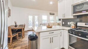 A modern kitchen with white cabinetry, a stainless steel refrigerator, a gas stove, and a dining area with a wooden table and chairs. - LAKE ARCADE - 5bd 4bth, FAMILY FUN SPOT, 3 stories (Garfield)