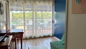 A room with a dining table, a sofa, and a view of a balcony with outdoor furniture. - 40m² With Terrace In A Residence With Pool (Le Grau-du-Roi)