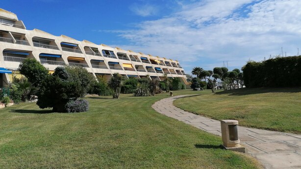 A multi-story hotel with a modern architectural design, featuring balconies and a well-maintained lawn with a pathway. - 40m² With Terrace In A Residence With Pool (Le Grau-du-Roi)