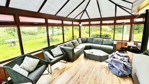 Une véranda avec un canapé modulable, des fauteuils en osier et une table.