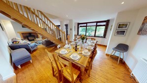 Un coin repas avec une table en bois dressée pour six personnes, un escalier et une vue sur la verdure à l’extérieur.