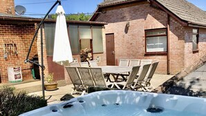 Un jacuzzi dans un jardin, avec une maison en briques, une table de patio et des chaises.