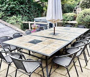 A square outdoor table with a tiled top, surrounded by black wicker chairs.