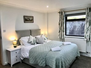 A neatly arranged bedroom with a bed, bedside tables, a window with curtains, and a wall-mounted picture.