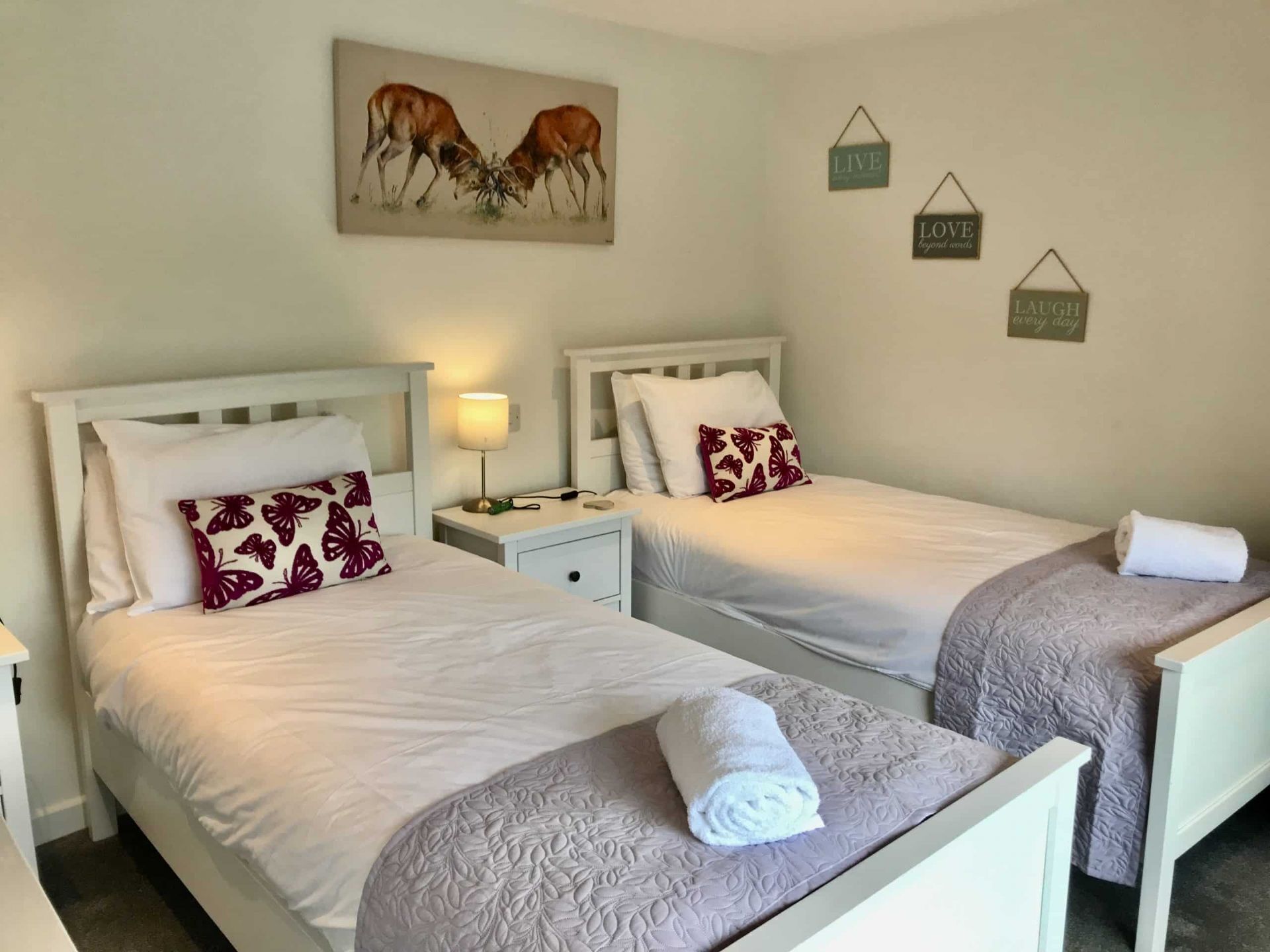 Una habitación de hotel con dos camas individuales, cabeceros blancos y un cuadro de ciervos en la pared.