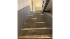 Una escalera con baldosas color crema y una barandilla, que conduce a una plataforma con un radiador.