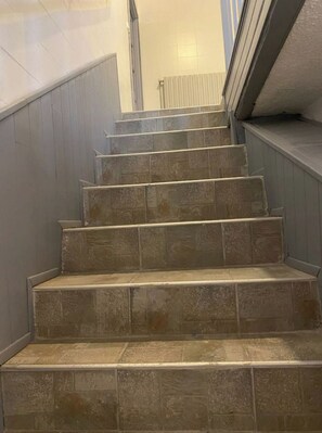 Een trap met beigetegels en een leuning, die uitkomt op een plateau met een radiator.