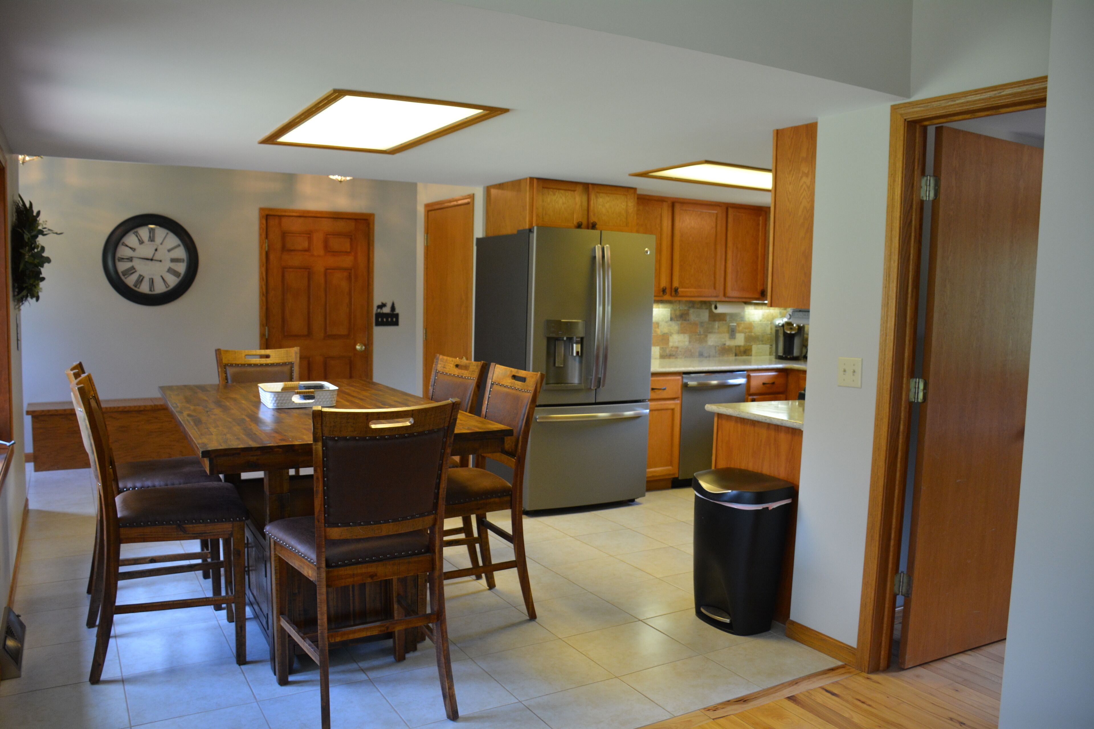 A modern kitchen with wooden cabinets, a stainless steel refrigerator, and a dining area with a wooden table and chairs.
