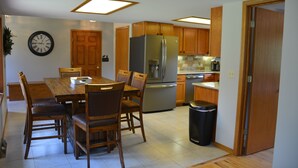 A modern kitchen with wooden cabinets, a stainless steel refrigerator, and a dining area with a wooden table and chairs.