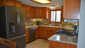 A kitchen with wooden cabinets, a stainless steel refrigerator, a dishwasher, a stove, and a water dispenser.