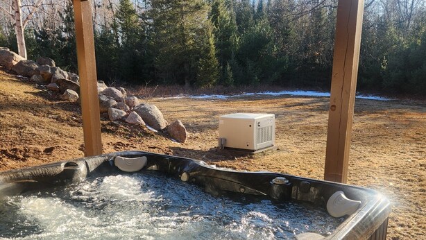 A hot tub under a wooden deck with a natural landscape in the background.