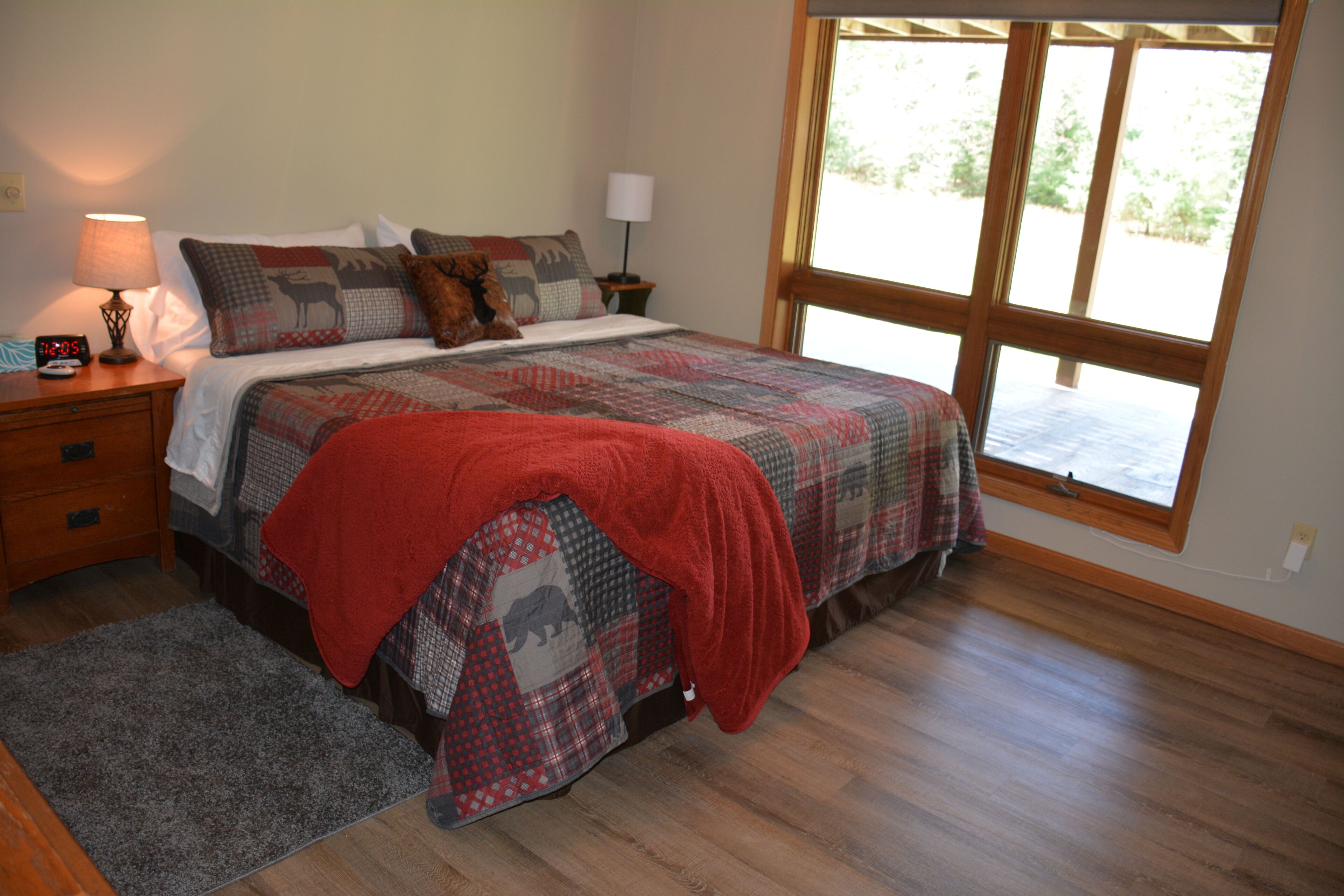 Een slaapkamer met een groot bed, een nachtkastje met lamp, een raam met uitzicht en een houten vloer.