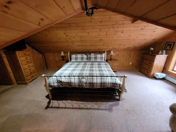 A bedroom with a wooden ceiling, a bed with a metal frame, a dresser, and a nightstand with lamps.