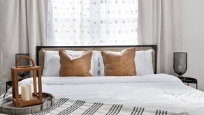 A neatly made bed with white linens and two brown pillows, a wooden lantern on the side, and a patterned throw blanket.