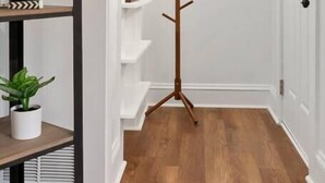 A hallway with a wooden floor, white walls, a round mirror on the wall, and a coat rack.