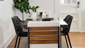 A dining area with a rectangular table, four chairs, a potted plant, and a door in the background.