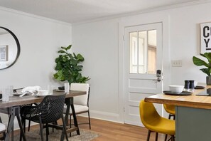 Uma área de refeições com uma mesa de madeira, cadeiras preto e branco, um vaso com planta e uma porta branca com espelho.