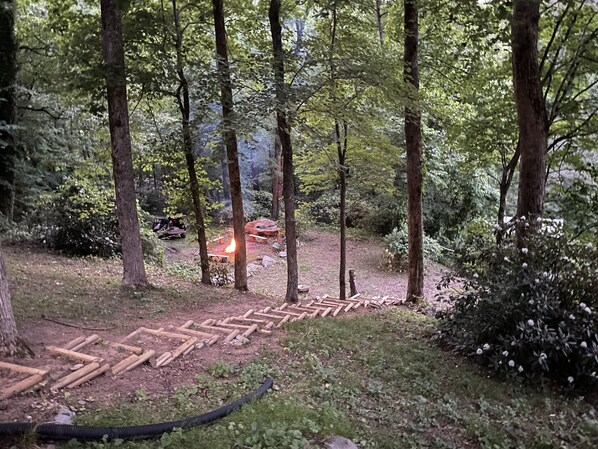 A forested area with a fire pit and a wooden structure, surrounded by trees and greenery. - Best View in Bat Cave (Hendersonville)