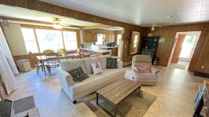 A spacious living room with a sofa, armchair, and coffee table. A kitchen is visible in the background with wooden cabinets and a dining area. - Best View in Bat Cave (Hendersonville)