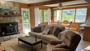 A cozy living room with a stone fireplace, a sofa, a coffee table, and a dining area with wooden furniture. - Best View in Bat Cave (Hendersonville)